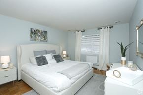New Brunswick apartment for rent - A white bedroom with a large bed and a nightstand with a plant on it.