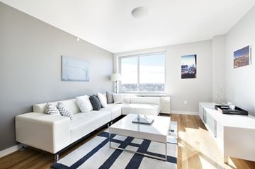 Woodside apartment for rent - A white couch with pillows sits in a living room with a large window.