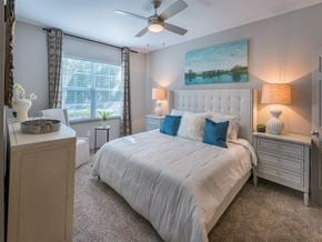 Tallahassee apartment for rent - Furnished bedroom with queen size bed, two night stands, large windows, ceiling fan, high ceiling and carpet flooring at Evergreens at Mahan in Tallahassee, FL
