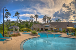 Tallahassee apartment for rent - Resort-style swimming pool with lounge chairs with view of the resident clubhouse at Lullwater at Blair Stone apartments for rent in Tallahassee, FL