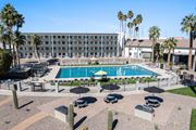 Tucson apartment for rent - A pool surrounded by chairs and umbrellas with a building in the background at Presidio Palms Apartments, Tucson, AZ, 85701