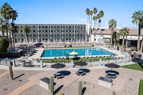 Tucson apartment for rent - A pool surrounded by chairs and umbrellas with a building in the background at Presidio Palms Apartments, Tucson, AZ, 85701