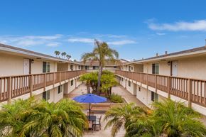 5151 Neptune Square Oxnard apartment for rent - A balcony with a blue umbrella and a pool in the middle of the courtyard.