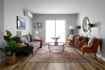Kamloops apartment for rent - A living room with a grey couch, a red throw, a round table with a plant on it, a chair, a rug, and a mirror on the wall.