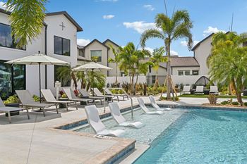 A pool with chairs and umbrellas in front of a building.