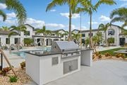 North Port triplex for rent - A modern outdoor kitchen with a grill and sink is set up in front of a row of houses at The Hadley - North Port, FL Apartments, North Port