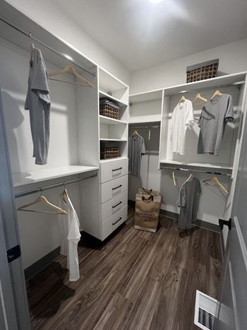 A walk in closet with white cabinets and wooden floors