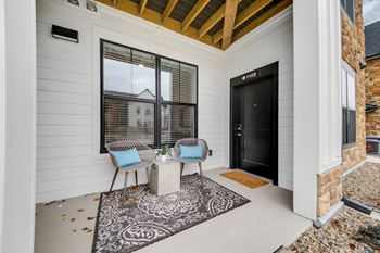 The front porch of a home with two chairs and a table and a black door
