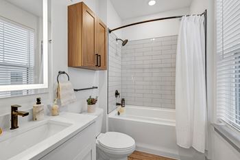 A white bathroom with white subway tile and a shower and a sink and a toilet