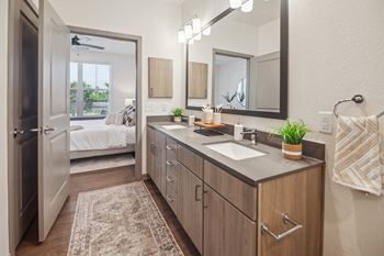 A bathroom with a sink and a mirror and a door to a bedroom