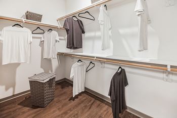 A walk in closet with white clothes and a wood floor