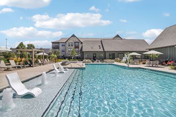 A swimming pool with chairs and a building in the background 