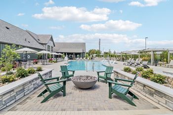 A swimming pool with green chairs and a fire pit 