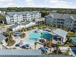 Lady Lake apartment for rent - A large swimming pool surrounded by palm trees and lounge chairs in front of apartment buildings at Standard441 Luxury Apartments, Lady Lake, Florida