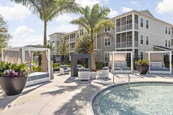 A pool area with a hot tub and lounge chairs in front of a multi-story apartment building