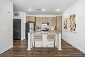 A kitchen with a refrigerator, oven, and a counter with two chairs