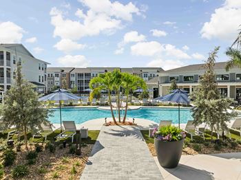 A pool surrounded by trees and chairs with a building in the background