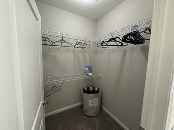A walk in closet with a trash can and hanging racks