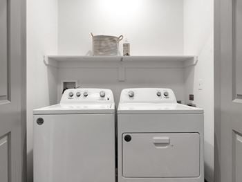 A white washer and dryer in a white laundry room with a shelf above