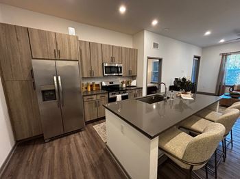 A modern kitchen with a refrigerator, microwave, oven, sink, and bar stools.