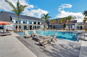 A swimming pool with lounge chairs and a coffee table in front of a building with palm trees