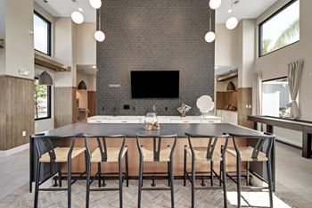 A large dining table with chairs in front of a kitchen with a large tv on the wall