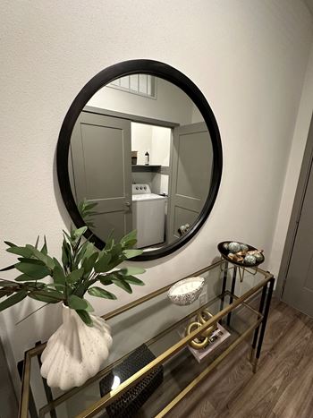 A round mirror above a glass table with a vase on it