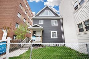 Winnipeg triplex for rent - a gray house with a gray roof behind a chain link fence and next to a brick building