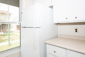 Winnipeg apartment for rent - A white refrigerator in a kitchen with a window showing a view of a house and a lawn.