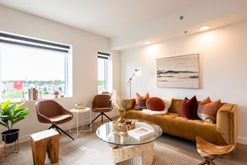 Winnipeg apartment for rent - A living room with a brown sofa, a glass table, and a painting on the wall.