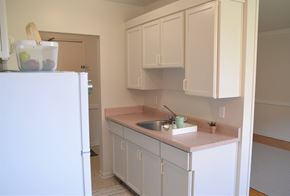 Winnipeg apartment for rent - Compact kitchen with white cabinets, pink countertops, and view of the entry door at 359 Edison.