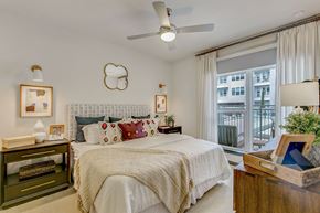 Fort Worth apartment for rent - A bedroom with a large bed, a ceiling fan, and a window with a view of a balcony.