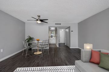Orlando apartment for rent - A living room with a grey couch, a dining table with chairs, a ceiling fan, and a rug on the floor.