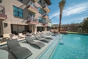 San Antonio apartment for rent - A pool with lounge chairs and umbrellas in front of a building with balconies.