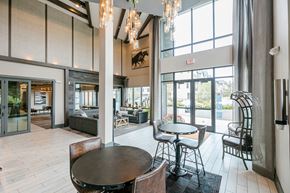 Dallas apartment for rent - A large room with a table and chairs in the foreground and a balcony with a view of the city in the background.