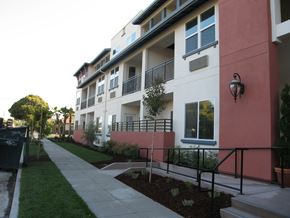 Santa Clara apartment for rent - A building with a red and white facade has a balcony and a small garden in front.
