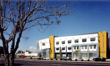 San Jose apartment for rent - A modern building with a yellow and white facade is surrounded by trees and cars.