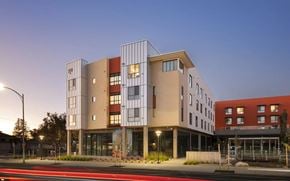 San Jose apartment for rent - A modern building with a mix of beige and red colors is illuminated by street lights.