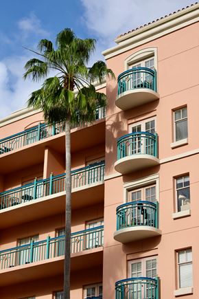 San Jose apartment for rent - A tall pink building with balconies and a palm tree in front.