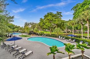 Plantation apartment for rent - A pool surrounded by palm trees and lounge chairs.