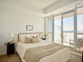Ottawa apartment for rent - A bedroom with a large bed and a view of the ocean through the sliding glass doors.