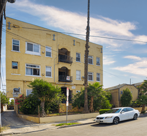 Los Angeles apartment for rent - A white car is parked in front of a yellow building with a balcony.