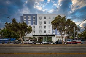 San Diego apartment for rent - A modern white building with blue trim is surrounded by trees and street lights.