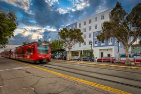 San Diego apartment for rent - A red train is passing by a white building.
