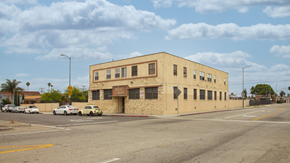 Los Angeles apartment for rent - A building with a yellow facade is situated on a street corner with cars parked in front.