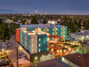 Los Angeles apartment for rent - A multi-story building with a mix of blue and orange hues stands out against the cityscape at dusk.
