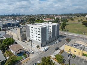 Los Angeles apartment for rent - A large grey building sits in the middle of a street with cars parked on the side.
