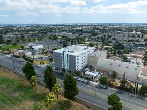 Los Angeles apartment for rent - A white building with a blue stripe is in the center of a city street.