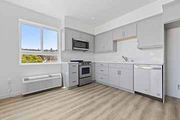 Los Angeles apartment for rent - A kitchen with white cabinets and appliances, a window with a view of the outdoors, and a wooden floor.