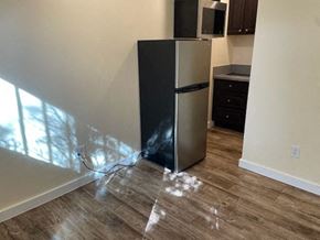 Los Angeles apartment for rent - A black fridge in a room with wooden flooring and sunlight coming through the window.